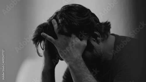 Dramatic depressed young man suffering from emotional pain. Somber closeup face of a male person in 30s feeling sadness and lost in monochromatic black and white photo