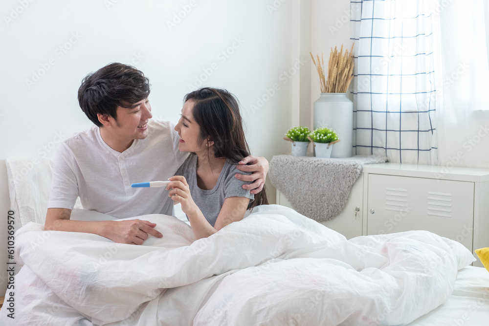 Young Asian Couple Embrace Heartwarming Moment - Sharing the Exciting News of Pregnancy Results on a Cozy White Bed in Their Bedroom, Capturing the Joy and Anticipation of Starting a Family, Ideal for Young Asian Couple Embrace Heartwarming Moment - Sharing the Exciting News of Pregnancy Results on a Cozy White Bed in Their Bedroom, Capturing the Joy and Anticipation of Starting a Family, Ideal for