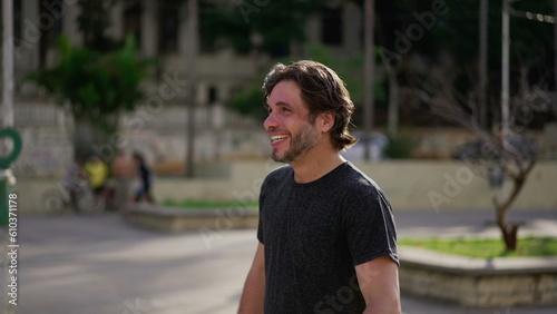 One happy handsome young man smiling and laughing while standing outside in city park. Authentic laugh and smile of a male caucasian person candid expression
