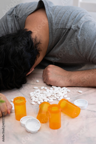 Vertical image of man passed out on table with many drugs pills in front of him