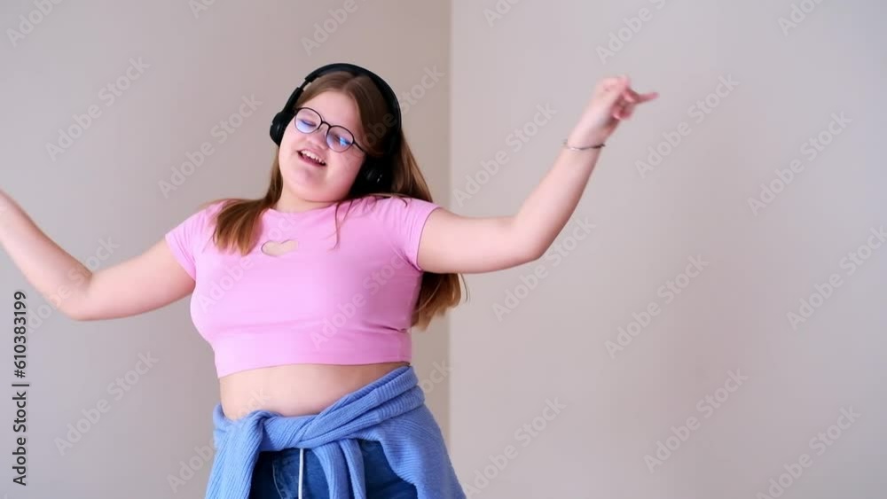 TikTok blogger in glasses dancing to music on camera following contemporary trends active overweight teen girl in headphones having fun in room at home