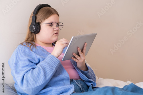 Relaxed teen girl in headphones completing online tasks on school website via modern tablet focused teenager in black-rimmed glasses studying online at home photo