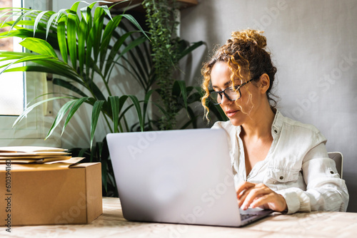 Professional freelance businesswoman working at home office with laptop and wearing glasses. Concept of business start-up online. Package for shipment on the table. Busy entrepreneur new job concept photo