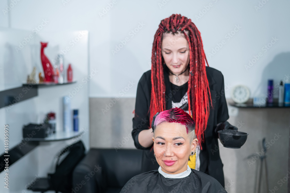 The hairdresser dyes the hair of an Asian woman in pink. Short extreme haircut. 