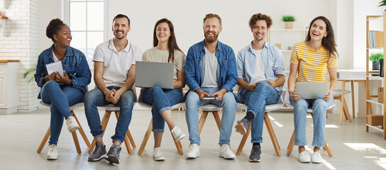 DIverse team of happy modern corporate company workers having fun at work. Group of joyful mixed race multiethnic people in T shirts and jeans with laptops and notebooks sitting in office and laughing