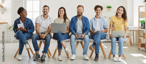 DIverse team of happy modern corporate company workers having fun at work. Group of joyful mixed race multiethnic people in T shirts and jeans with laptops and notebooks sitting in office and laughing
