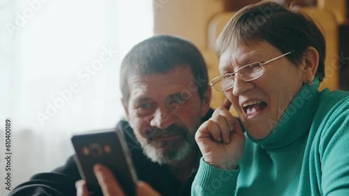 Happy parents look at the phone while sitting in the living room and smile.