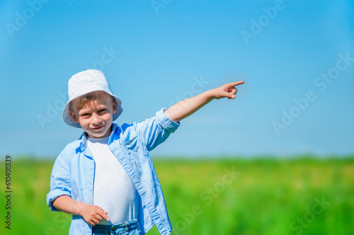 Portrait of a smiling boy with a raised hand pointing to the blue sky, green grass in a light background, the concept of freedom, joy, success. space for text