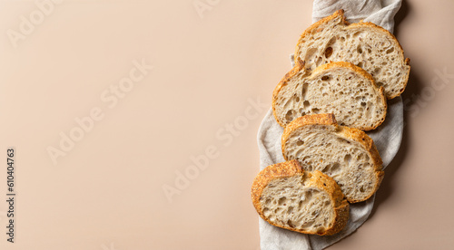 Sliced wheat rustic bread on a linen towel. Artisan bread cut into slices, wide banner with space for text on a beige background. Organic bakery products.