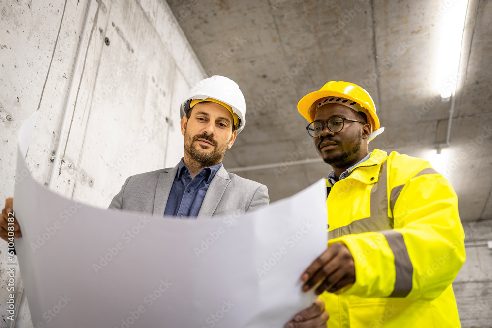 Construction worker and civil engineer checking blueprint plans together.