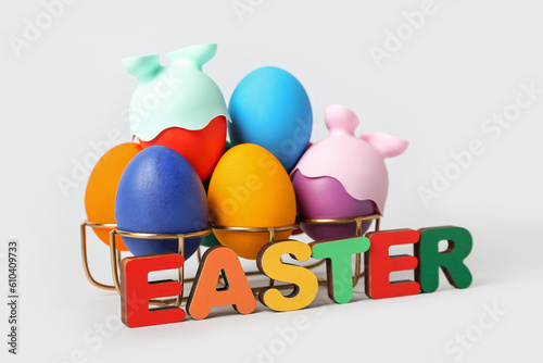 Holder with funny painted eggs and word EASTER on grey background