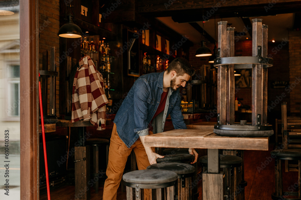 Happy Caucasian waiter opening the door at a cafe and preparing a venue in the morning. Happy Caucasian waiter opening the door at a cafe and preparing a venue in the morning.