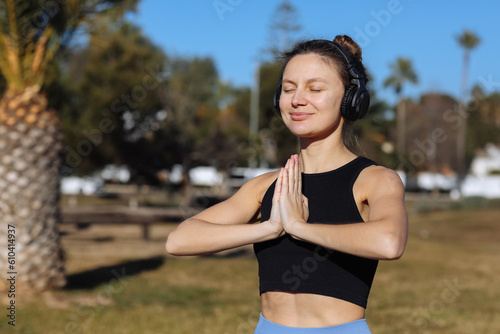 Young healthy woman in sportswear listens music in headphones while doing fitness squat leg exercises outdoors in park with palm trees. Workout for strengthen pelvic floor muscles on summer holiday © Andriy Medvediuk