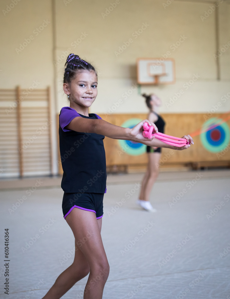 Girl trainee doing workout with rope on rhythmic gymnastics training with  other trainees in gym in sports camp Stock Photo