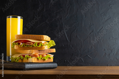 Fresh orange juice and a sandwich of toasted lettuce, tomato, ham and cheese on a wooden table and rustic black background with free space for text