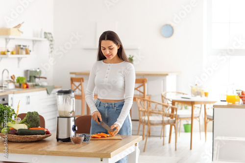Young woman cutting orange in kitchen