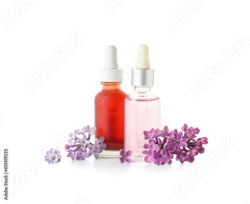 Bottles of cosmetic oil with beautiful lilac flowers on white background