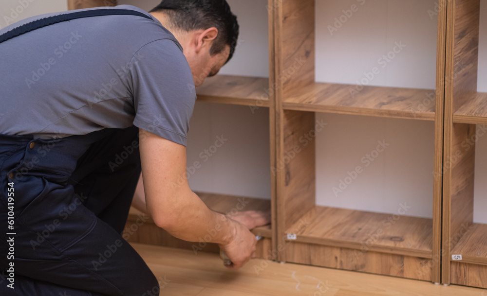 Managing carpentry business man in overalls assembling wooden rack with shelves specialist works with new high-quality prefabricated furniture in apartment woodwork industry Managing carpentry business man in overalls assembling wooden rack with shelves specialist works with new high-quality prefabricated furniture in apartment woodwork industry