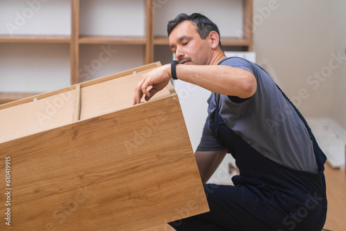 Furniture shipping and installation man lifting finished cabinet made of hardwood specialist in professional uniform assembling new furniture for home interior photo