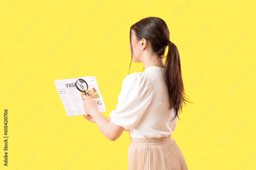 Young woman with magnifier reading newspaper on yellow background Young woman with magnifier reading newspaper on yellow background