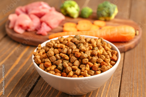Bowl with dry pet food on wooden background, closeup