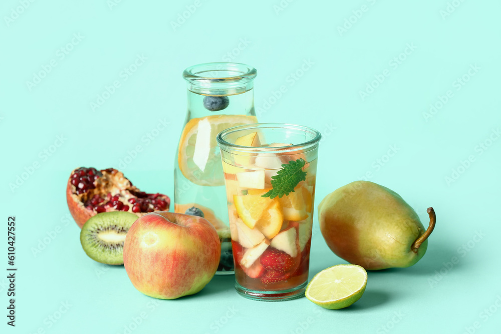 Glass and bottle of infused water with different sliced fruits on blue background Glass and bottle of infused water with different sliced fruits on blue background