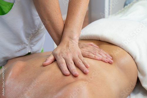 Hands of a physiotherapist in a crossed position, working on the back of a blonde woman, in a health clinic
