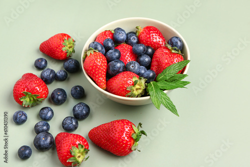 Bowl with fresh blueberries and strawberries on green background