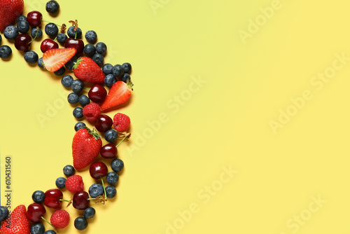 Frame made of different fresh berries on yellow background