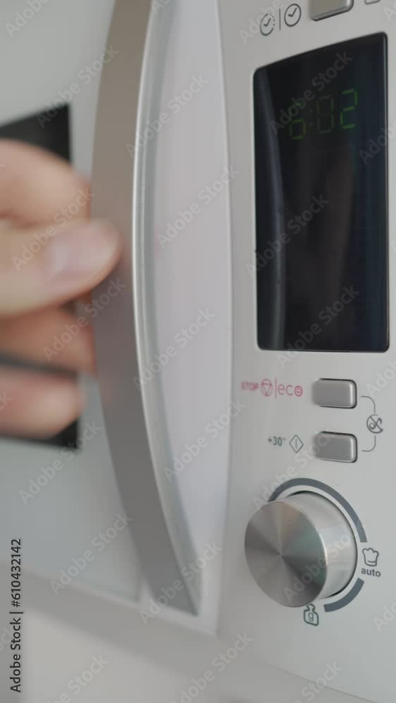 Close-up vertical video of a hand placing a cup in the microwave, pressing the operation button and turning the power knob. Close-up vertical video of a hand placing a cup in the microwave, pressing the operation button and turning the power knob.