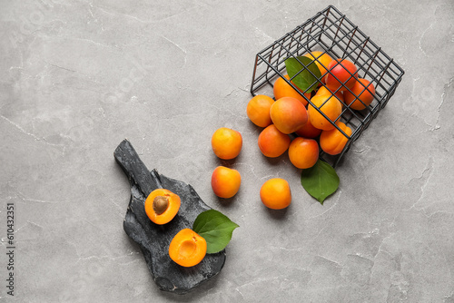 Basket and board with fresh apricots on grey background