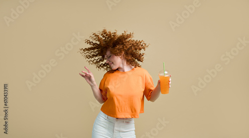 Photography Happy carefree young wavy-haired ginger woman dancing holding fresh juice drink