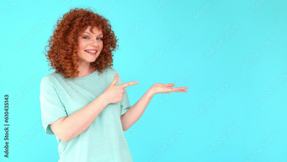 Positive young curly red-haired woman smiling pointing aside with hands at green copy space making suggestion and recommendation showing commercial advertisement workspace with empty place for text Positive young curly red-haired woman smiling pointing aside with hands at green copy space making suggestion and recommendation showing commercial advertisement workspace with empty place for text