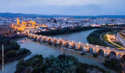 Scenic aerial view of lighted Roman bridge across Guadalquivir river and Mezquita-Catedral on background with Cordoba cityscape at twilight, Spain.. photo