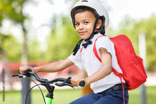 Happy ethnic child schoolboy in a helmet and with a briefcase rides a bike to school