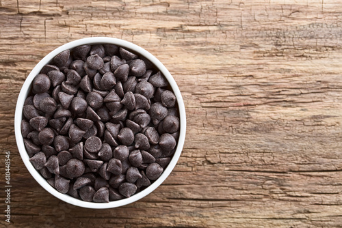 Chocolate chips or morsels in white bowl, photographed overhead on wood with copy space on the side (Selective Focus, Focus on the top chocolate chips)