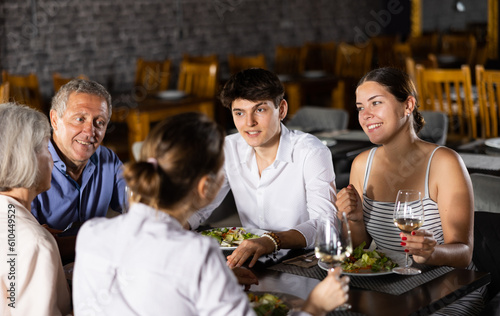 Elderly couple and young couple and adult woman have dinner and drink wine together in restaurant