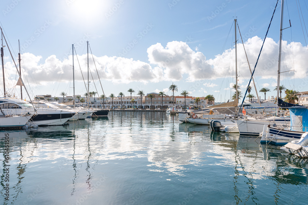 La Savina harbour, on the island of Formentera (Balearic Islands, Spain). Yachts and sailboats moored and the port's commercial promenade, with a line of palm trees, in the background,
