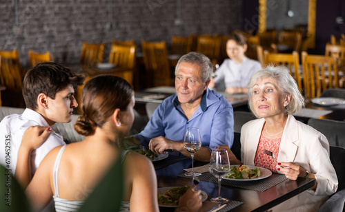 Elderly couple and young couple have dinner and drink wine together in restaurant
