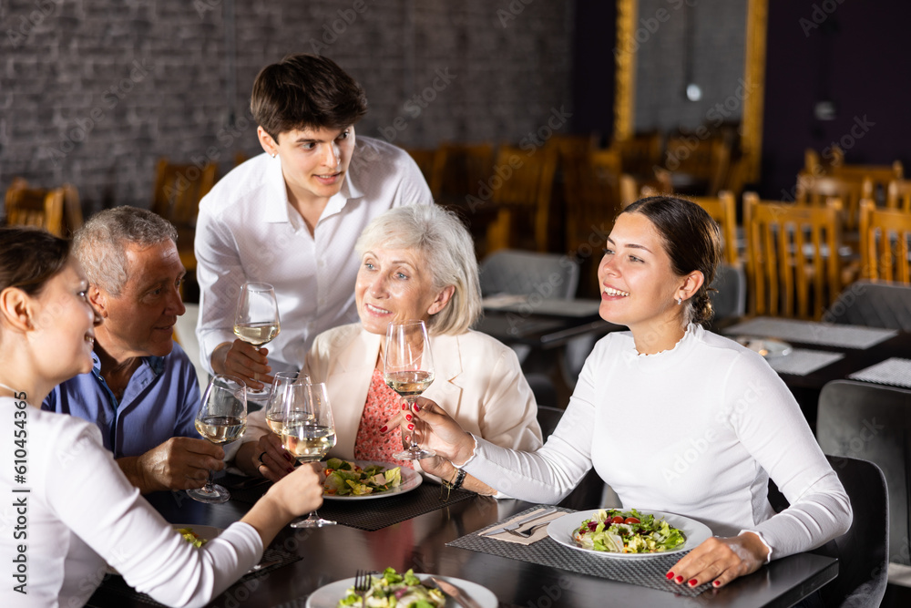 In cozy restaurant, elderly family and adult daughters with husband enjoy festive lunch, celebrating important event. They chat and taste wine, enjoying pleasant atmosphere and good company.