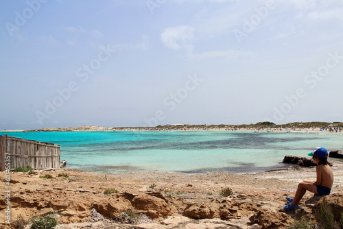 Little kid sitting close to sea shore in Ses Illetes beach, one of the most amazing and iconic spots of Formentera island, Spain.