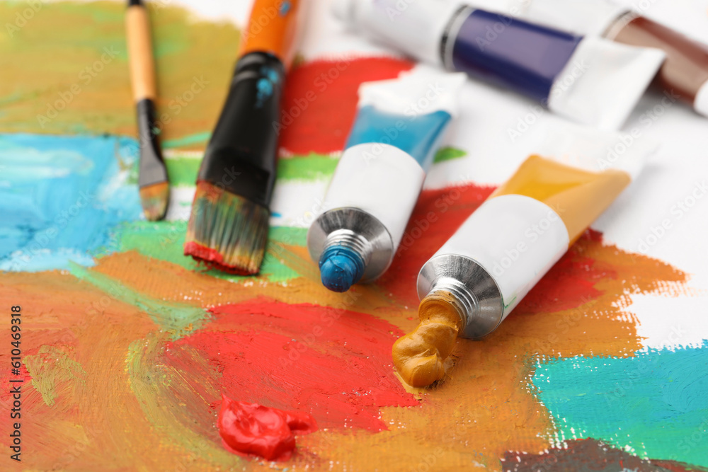 Tubes of colorful oil paints and brushes on canvas with abstract painting, closeup