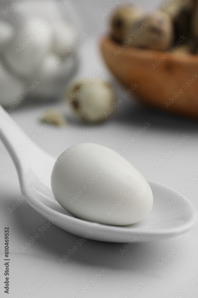 Fototapeta premium One boiled quail egg in spoon on white table, closeup