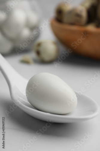 One boiled quail egg in spoon on white table, closeup