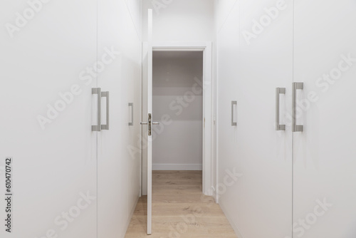 A walk-in closet with white wooden door cabinets on both