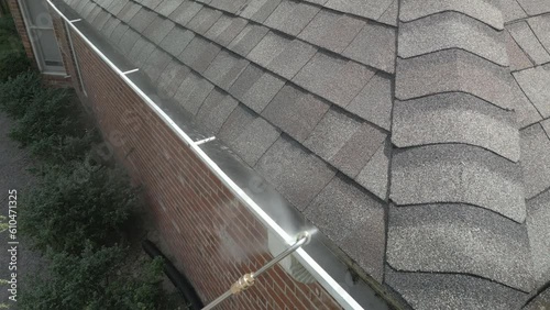 Cleaning dirty, metal gutters on a home using a pressure washer with long extension wand.