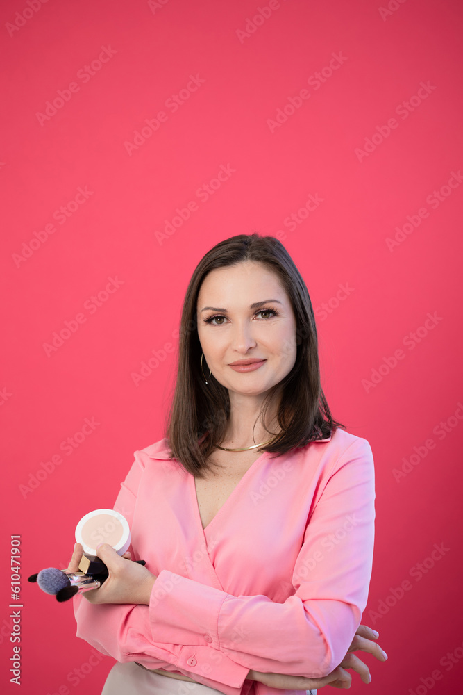Stylist and make-up artist, style and make-up studio, beauty industry. Stylish brunette with makeup in her hands, pink background Stylist and make-up artist, style and make-up studio, beauty industry. Stylish brunette with makeup in her hands, pink background