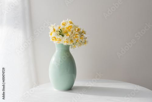 Close up of jonquils in green vase on small table next to curtain with copy space (selective focus)