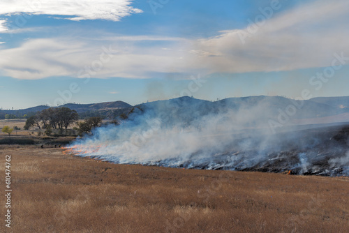 firefighters monitor a control burn in a large grass field in autumn