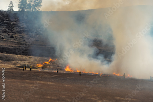 firefighters monitor a control burn in a large grass field in autumn